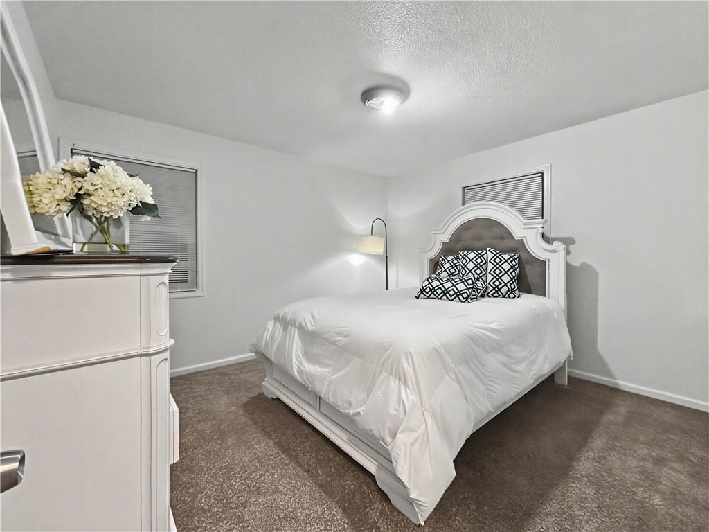 Bedroom with a white bed, ornate upholstered headboard, patterned pillows, and brown carpet.