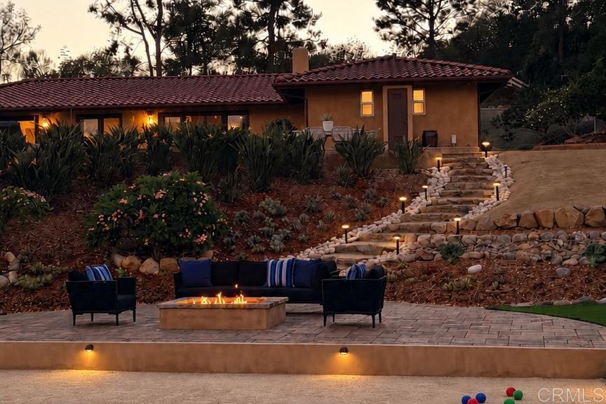 Home exterior with a landscaped hillside, stone steps, and a patio fire pit at dusk.