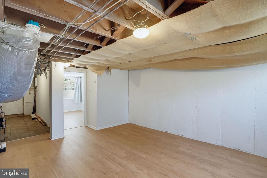Basement room with exposed ceiling insulation and light wood flooring.