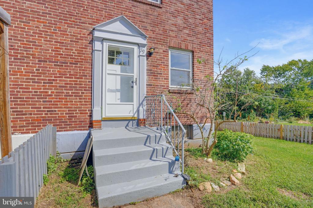 Brick house entrance with concrete steps, metal railings, and a fenced grassy yard.