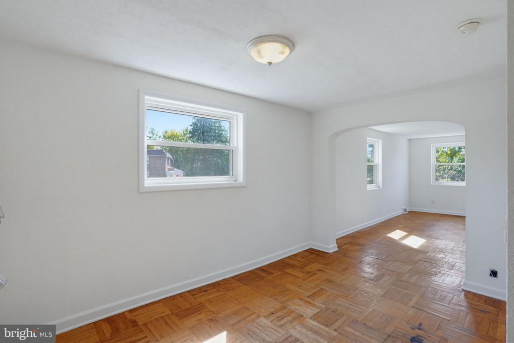 Empty room with parquet floors and an arched opening to a sunny adjoining room.