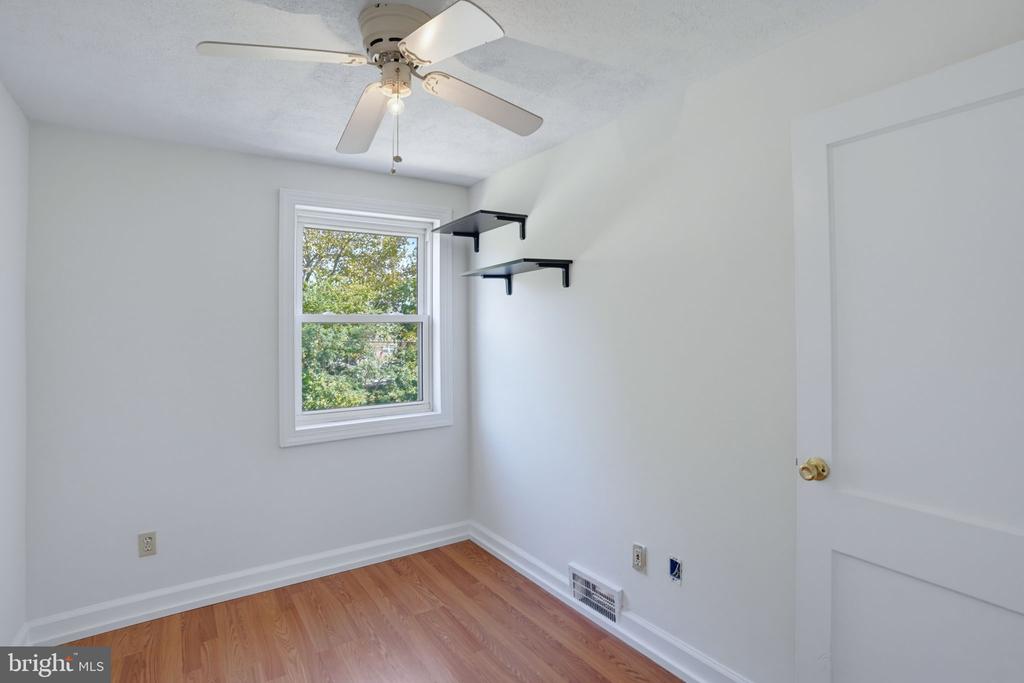 Empty room with hardwood floors, a ceiling fan, and a window overlooking trees.
