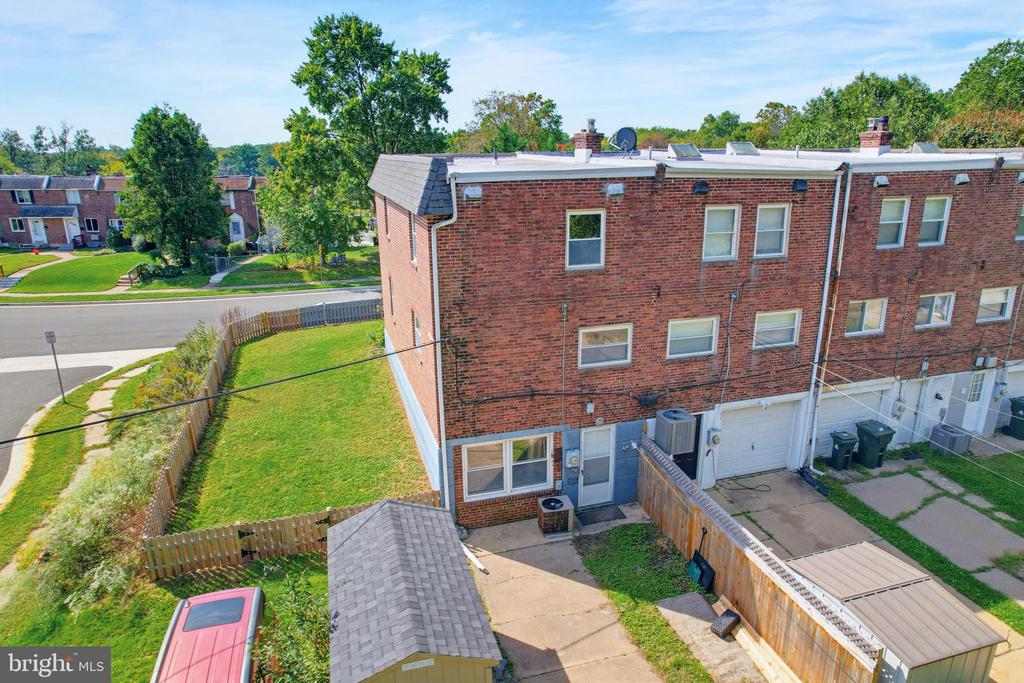 Aerial view of a red-brick townhouse, fenced grassy yard, and paved rear patio.