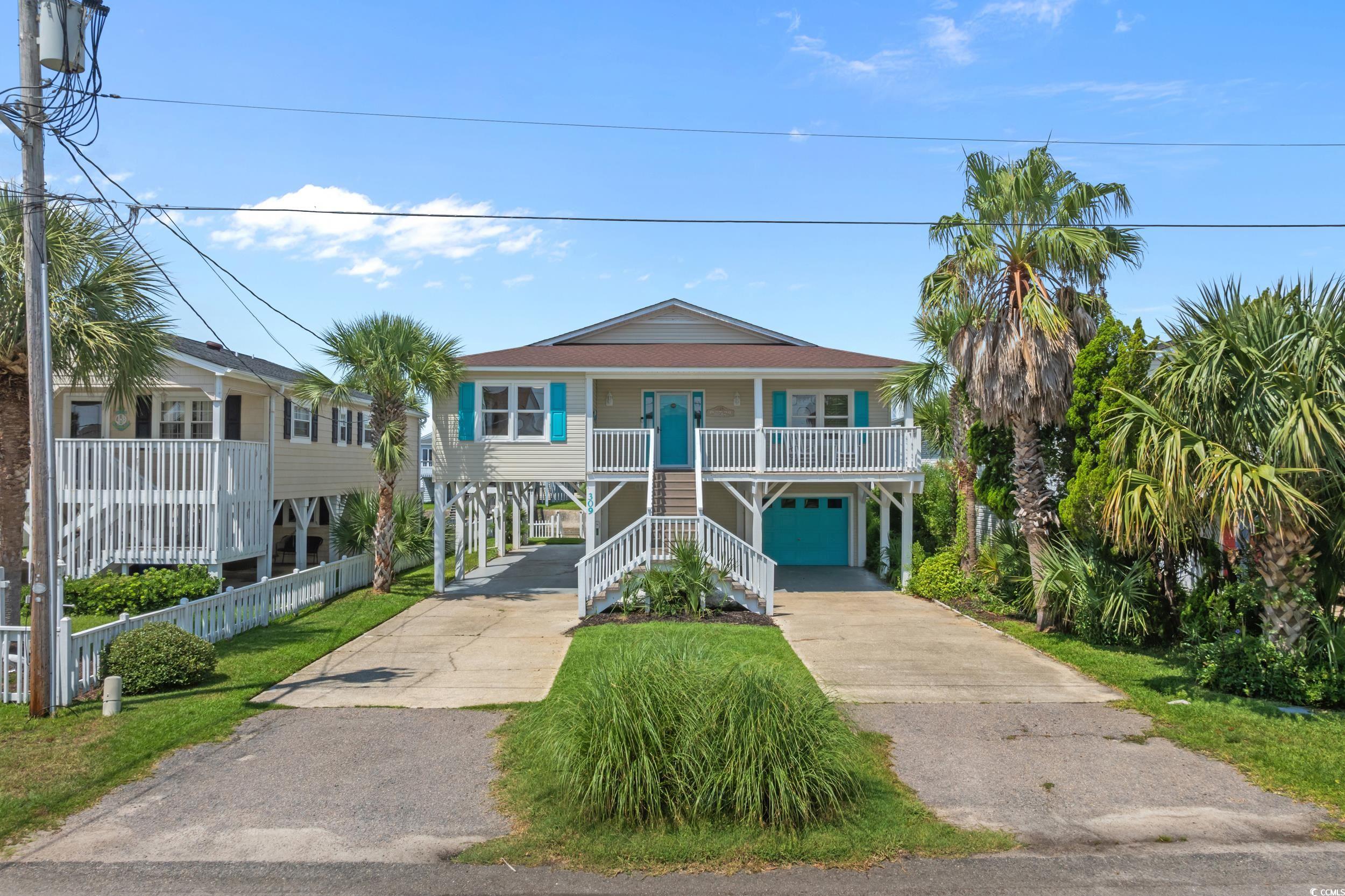 Raised coastal home with turquoise accents, white porch railings, and palm trees.