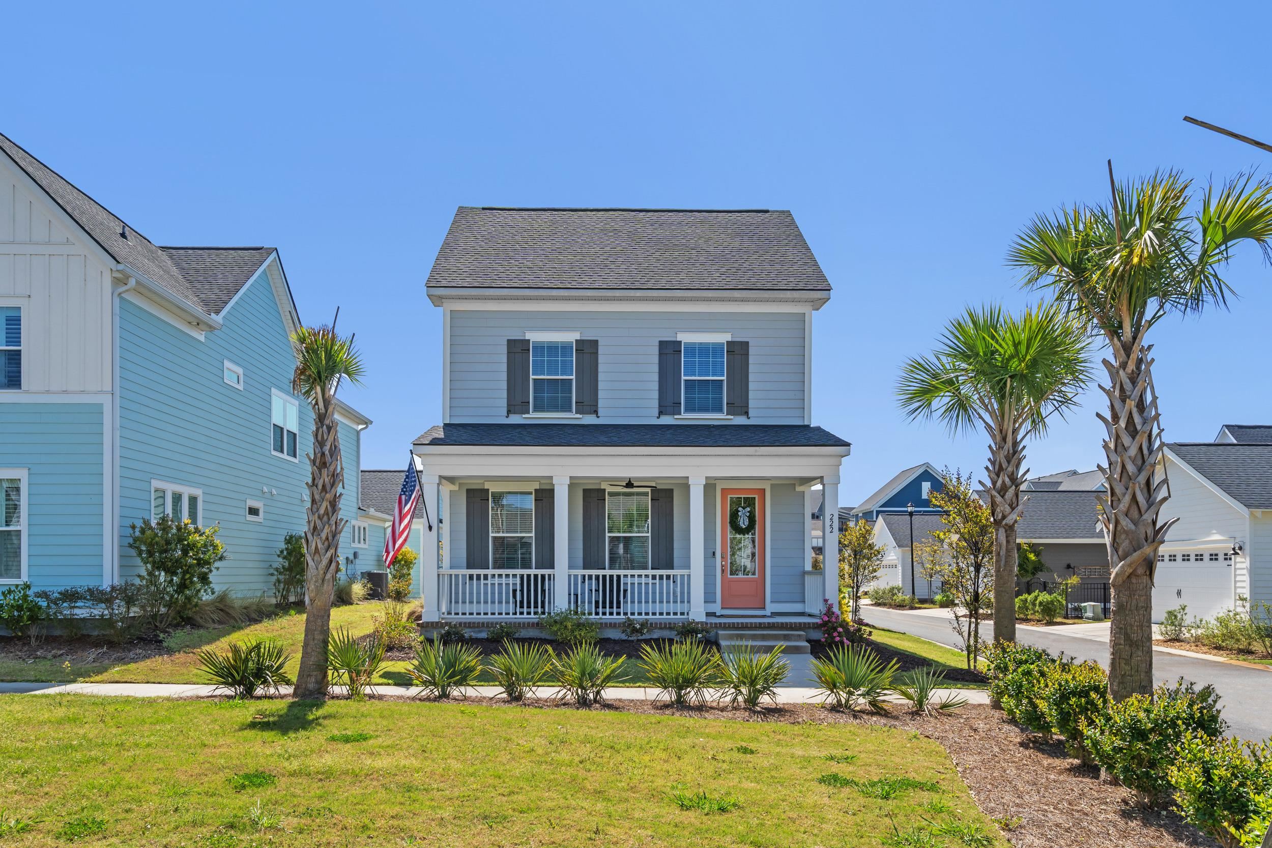 Light blue two-story house with a covered porch, coral front door, and palm trees.