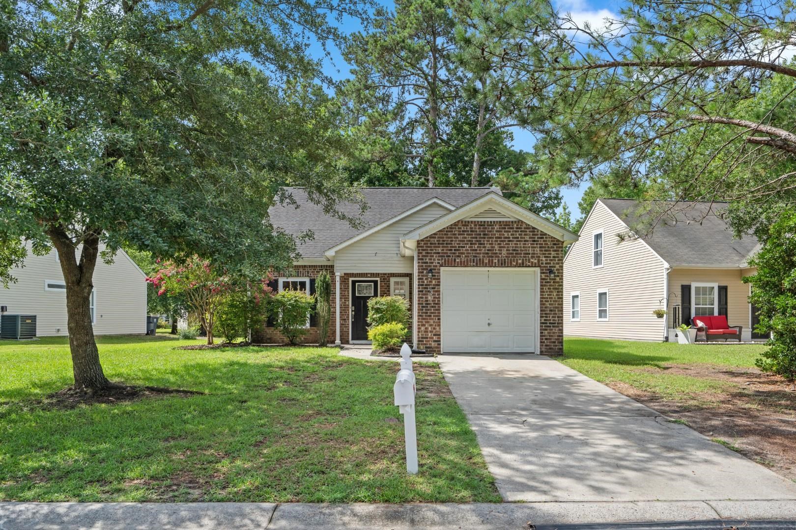 Brick-and-siding house with an attached garage, driveway, and white mailbox beneath mature trees.