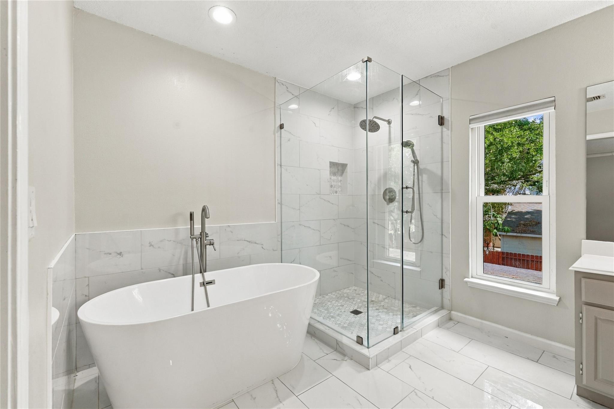 Bathroom with a freestanding soaking tub, glass-enclosed shower, and large window.