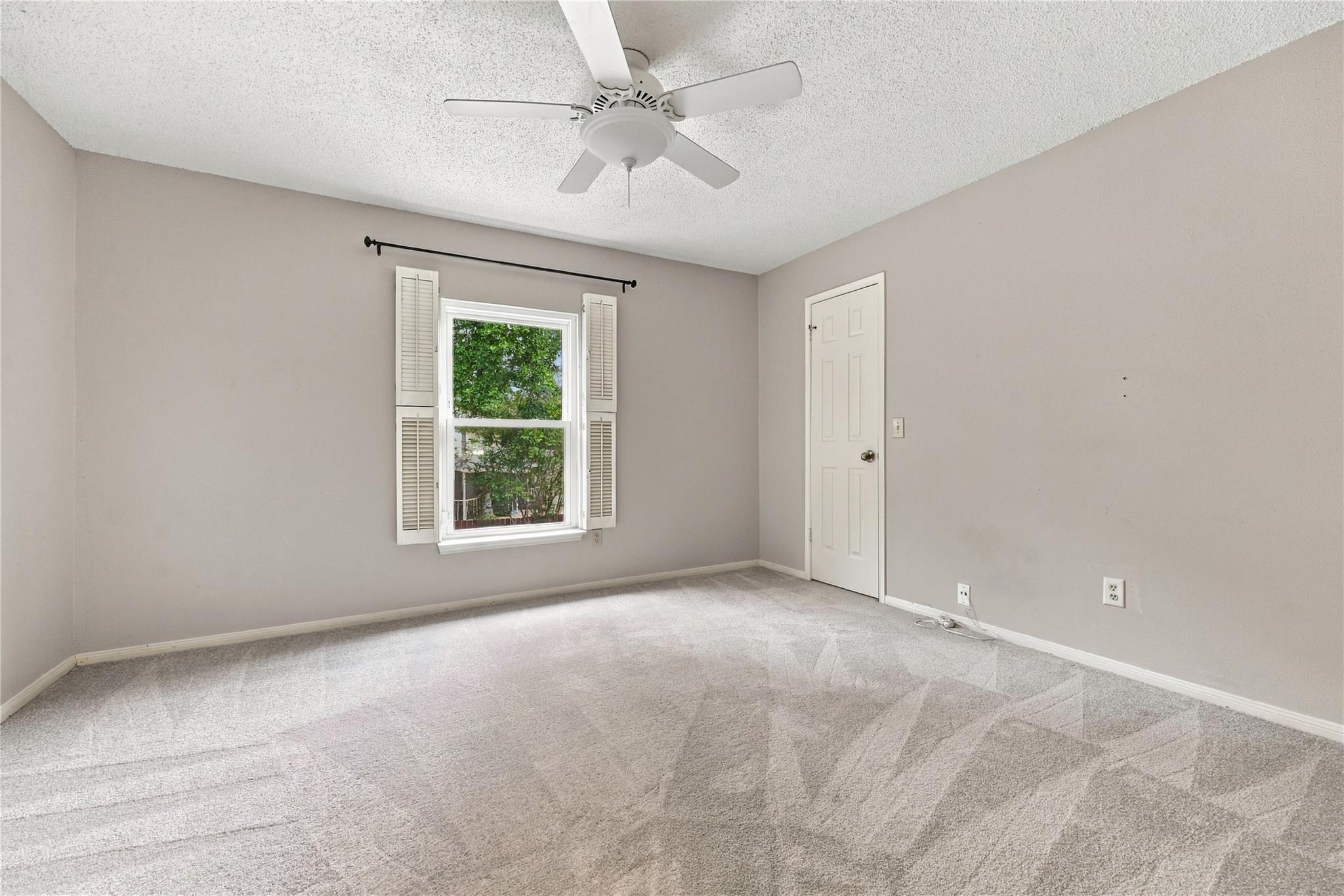 Empty bedroom with a ceiling fan and shuttered window.