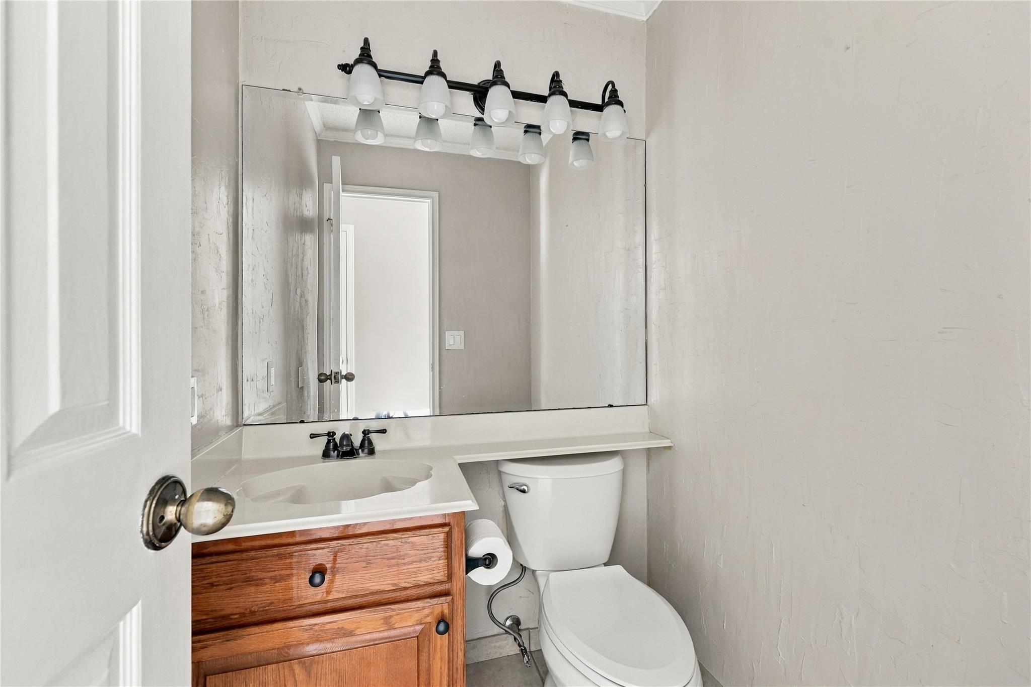 Compact bathroom with a wood-front vanity, large mirror, and white toilet.