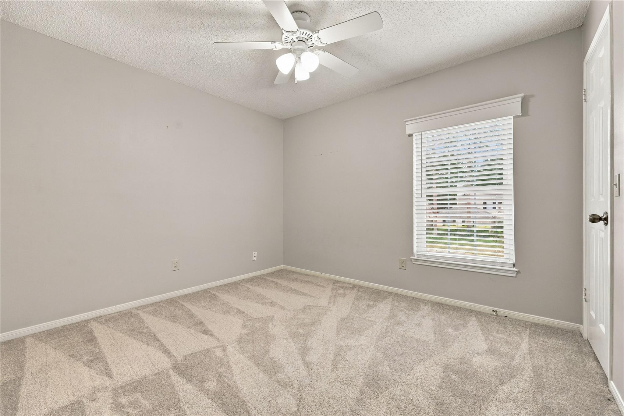 Empty carpeted bedroom with a ceiling fan, window blinds, and a white door.