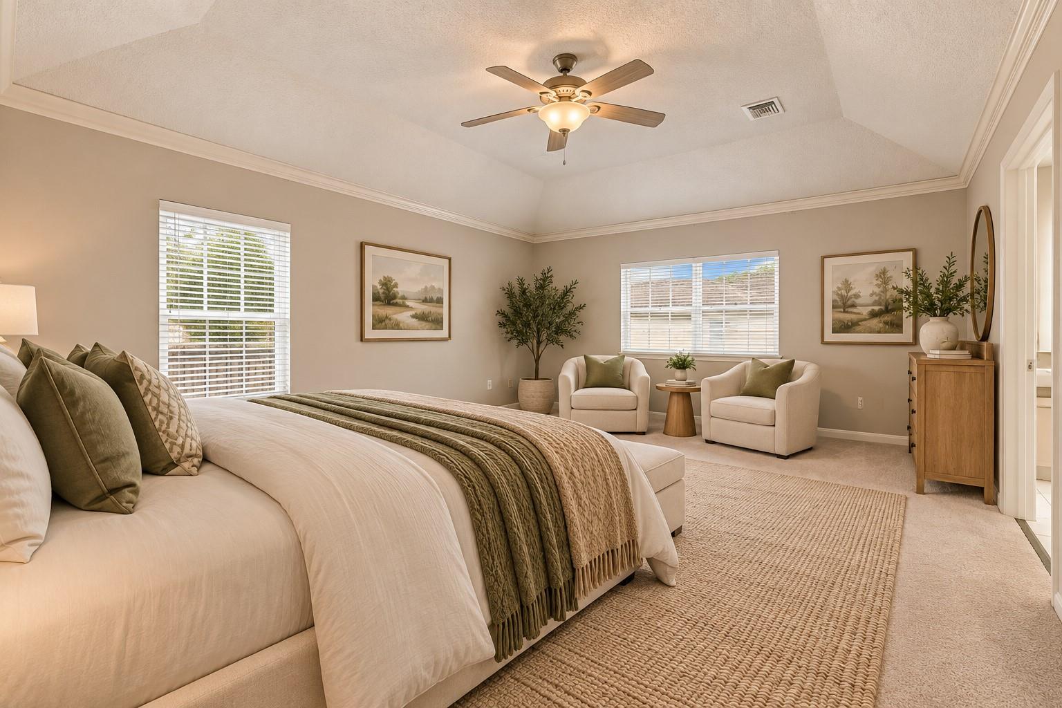 Furnished bedroom with a vaulted ceiling, large bed, and two armchairs by the windows.