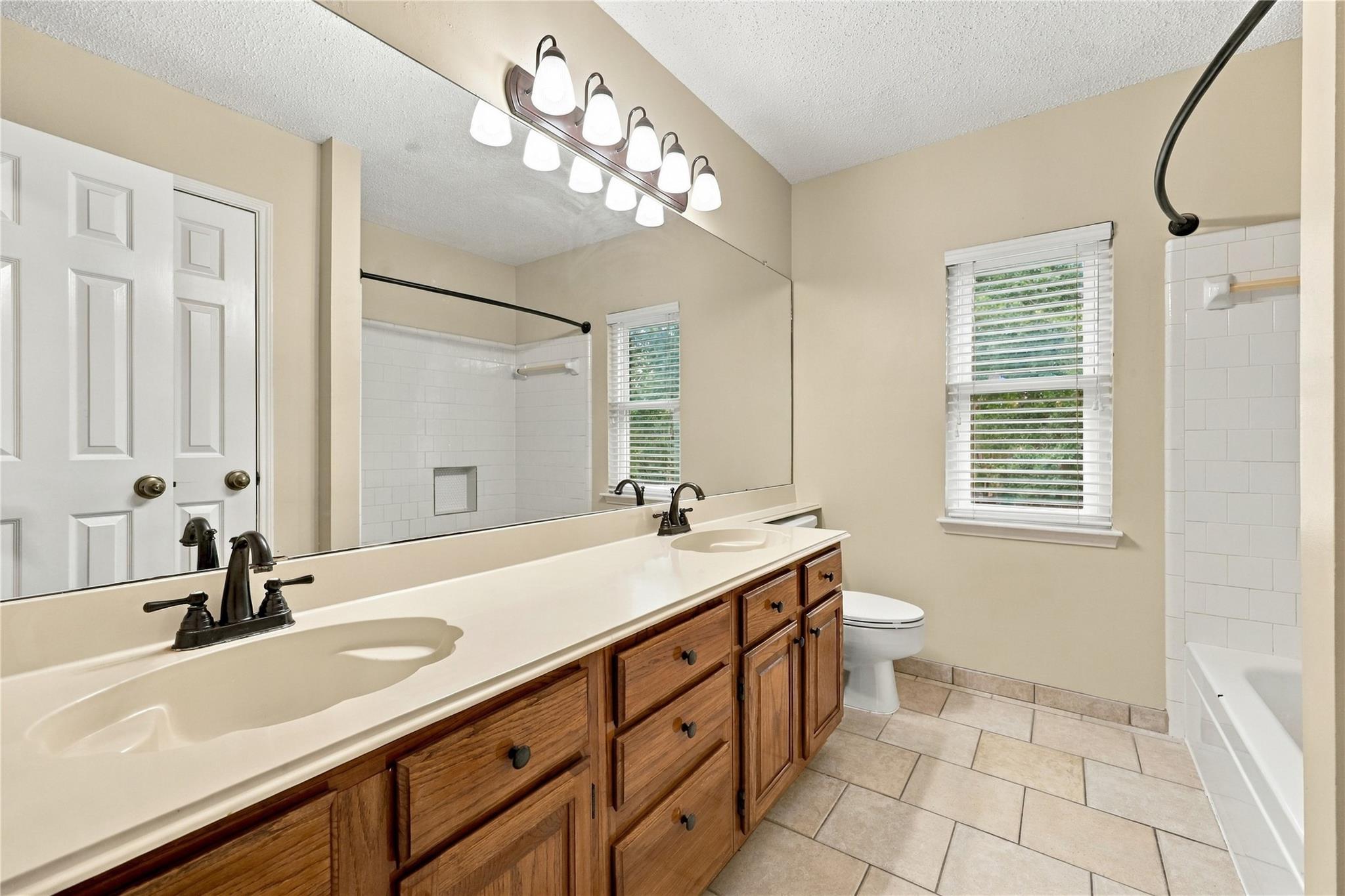 Bathroom with a long wooden double vanity, large mirror, and white-tiled tub and shower.