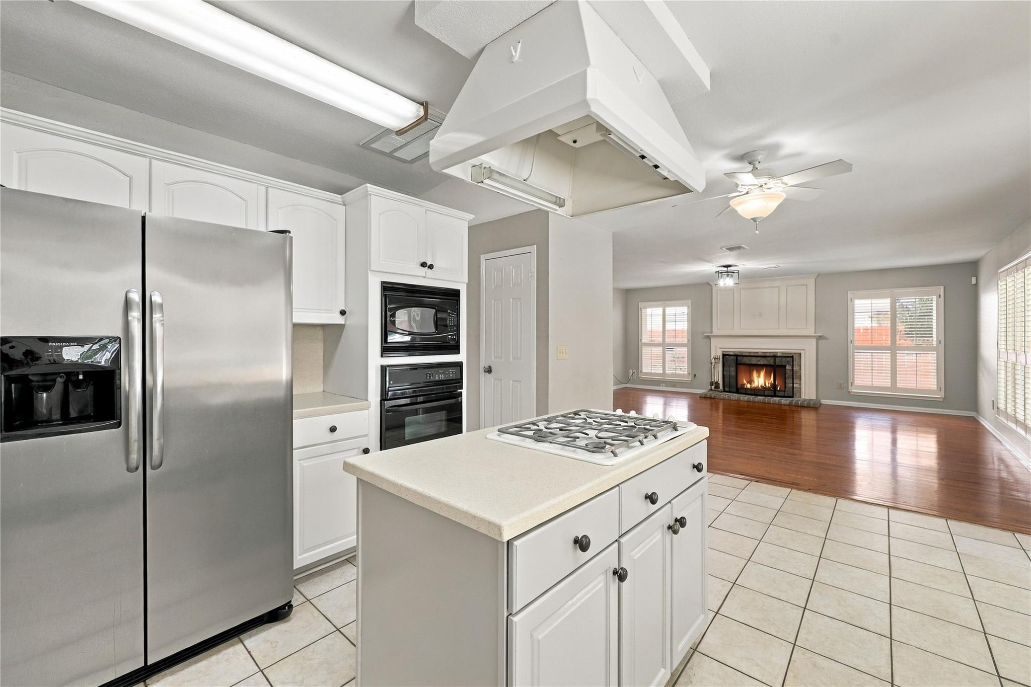 Kitchen with white cabinets, stainless steel appliances, and a central cooktop island opening to a fireplace living room.