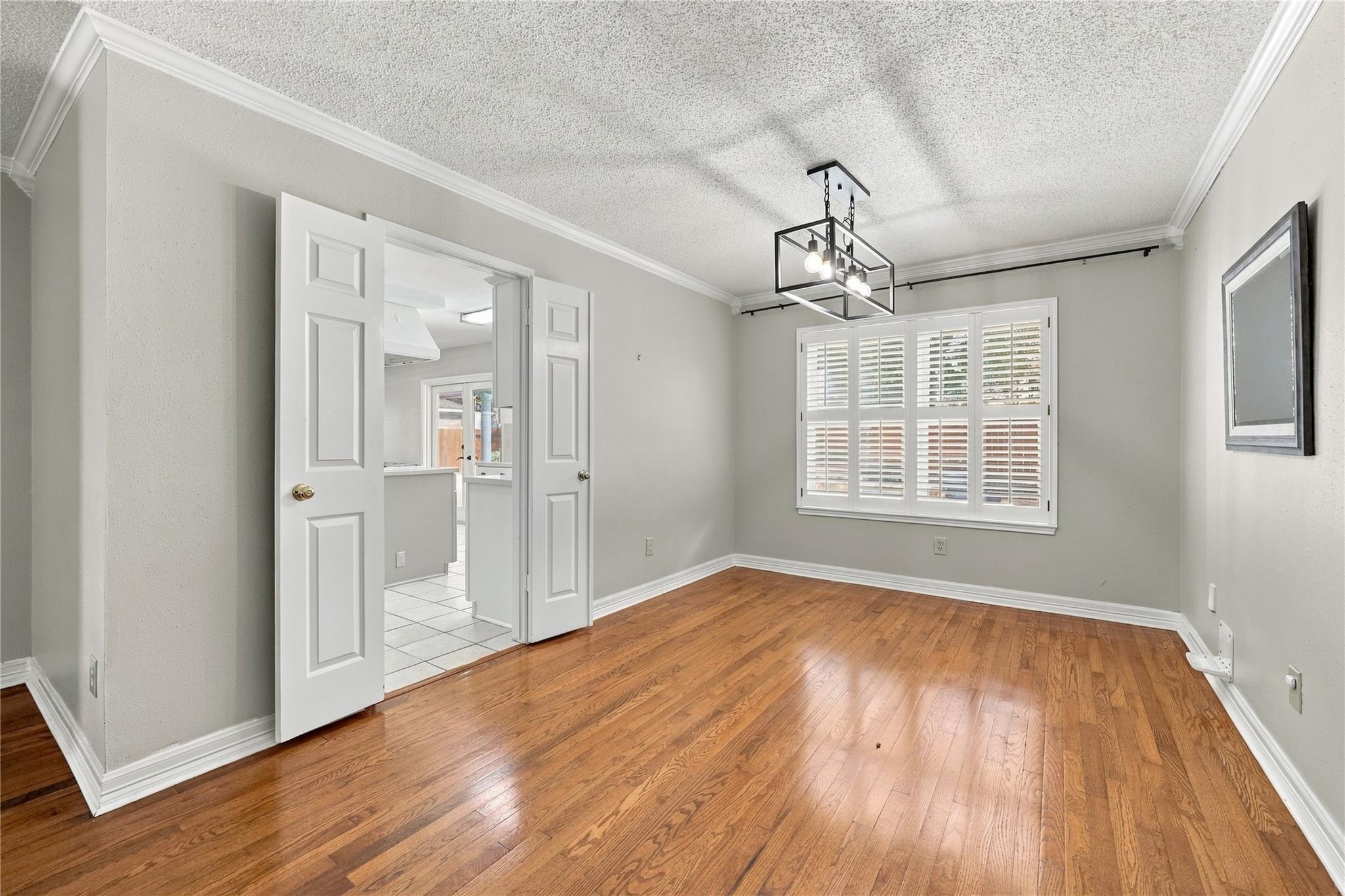 Empty dining room with hardwood floors, plantation shutters, and a geometric pendant light.