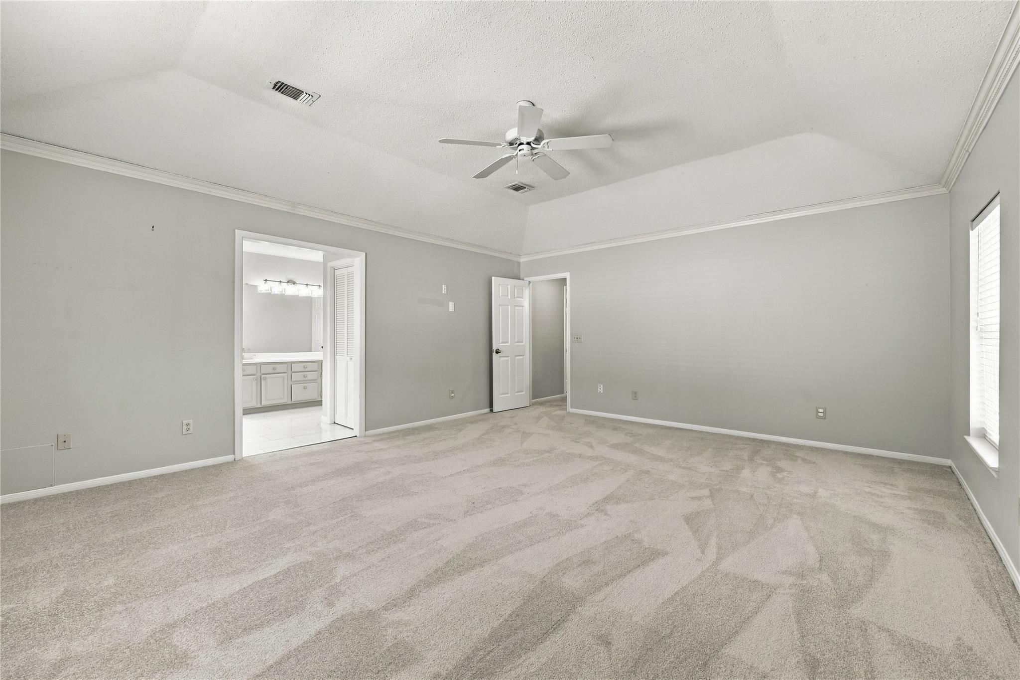 Vacant carpeted bedroom with a ceiling fan, window blinds, and an open doorway to the bathroom.