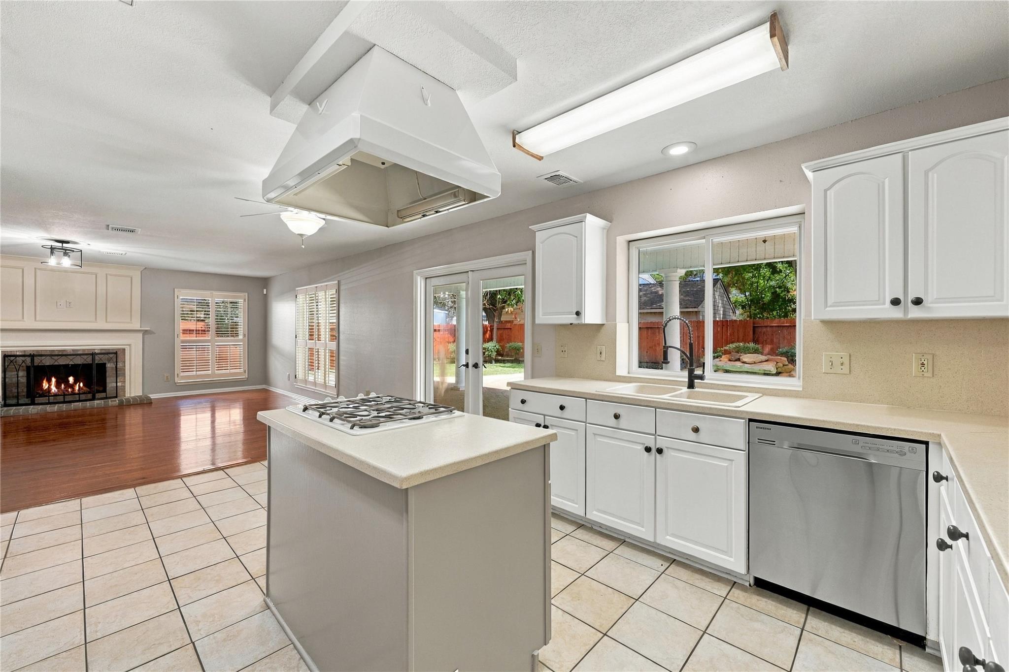 Kitchen with white cabinets, a gas cooktop island, and a window over the sink overlooking the backyard.