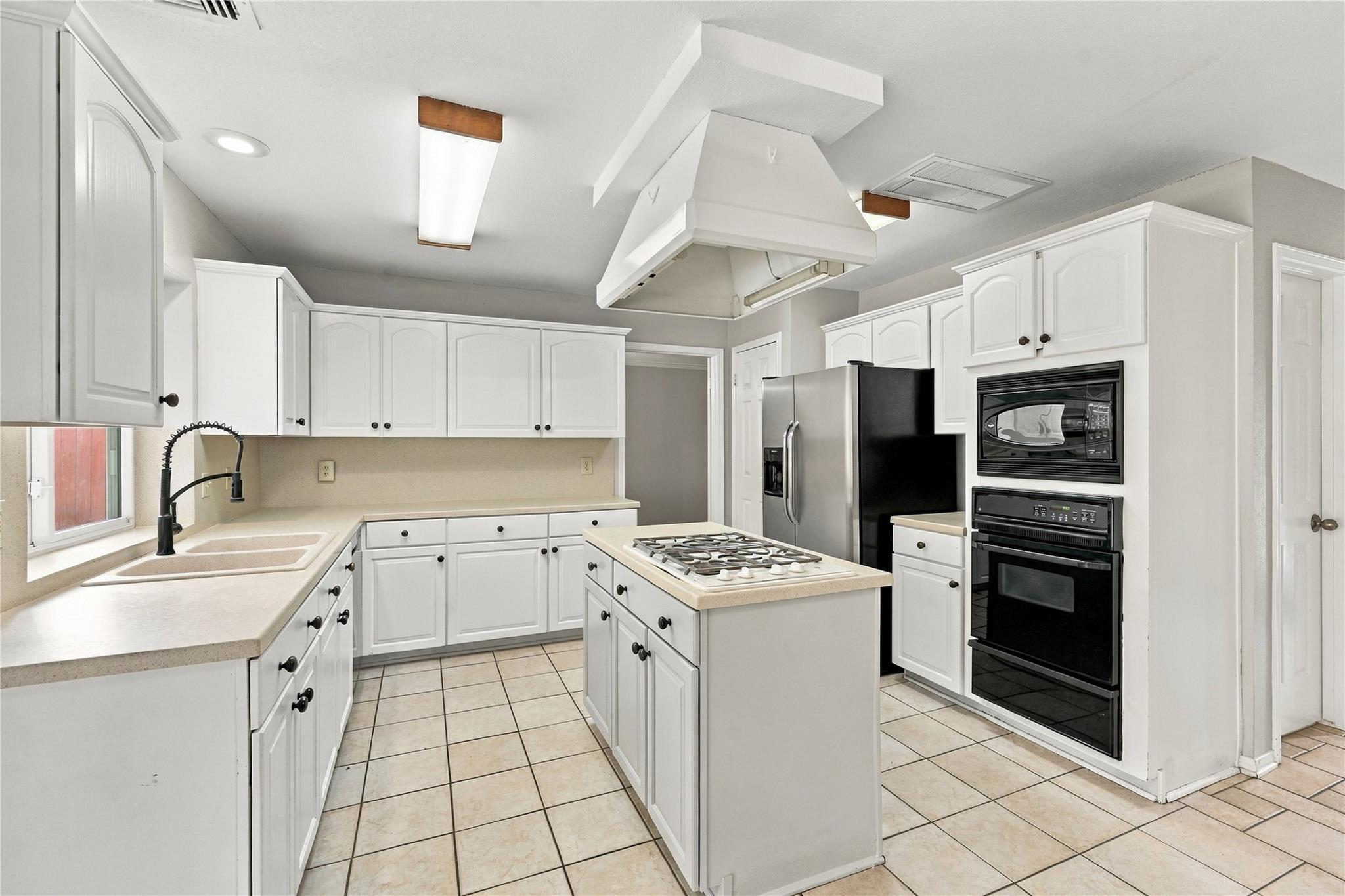 Kitchen with white cabinetry, a central gas cooktop island, and built-in black oven and microwave.