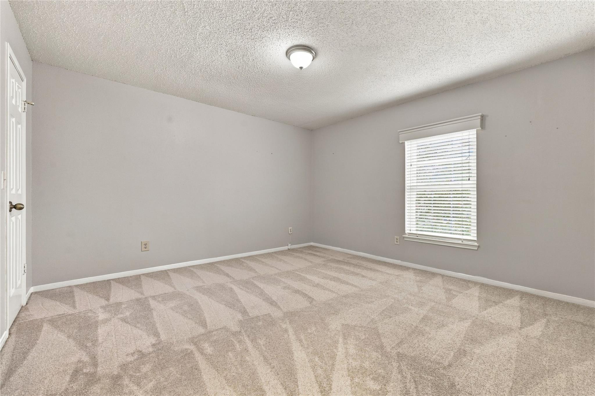 Vacant bedroom with beige patterned carpet and a window with white blinds.
