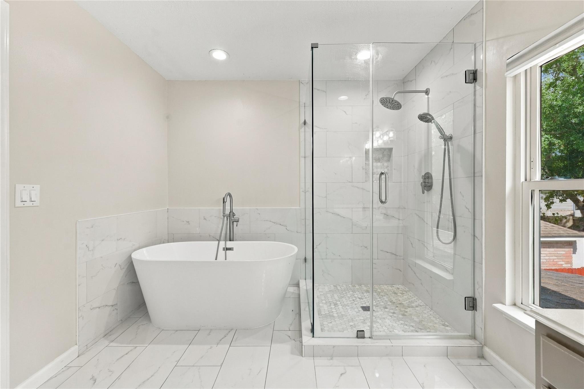 Bright bathroom with a freestanding tub and glass-enclosed shower beside a large window.