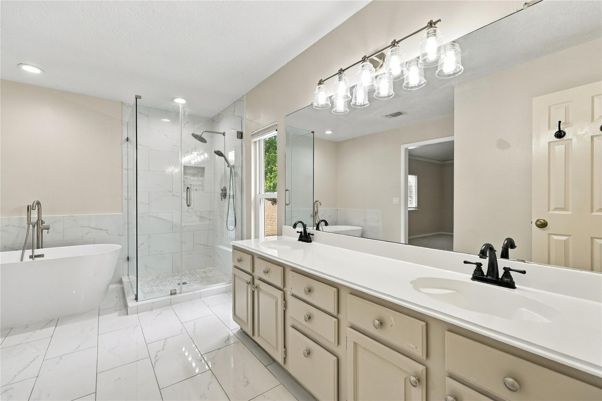Bathroom with double vanity, glass shower, and freestanding soaking tub.
