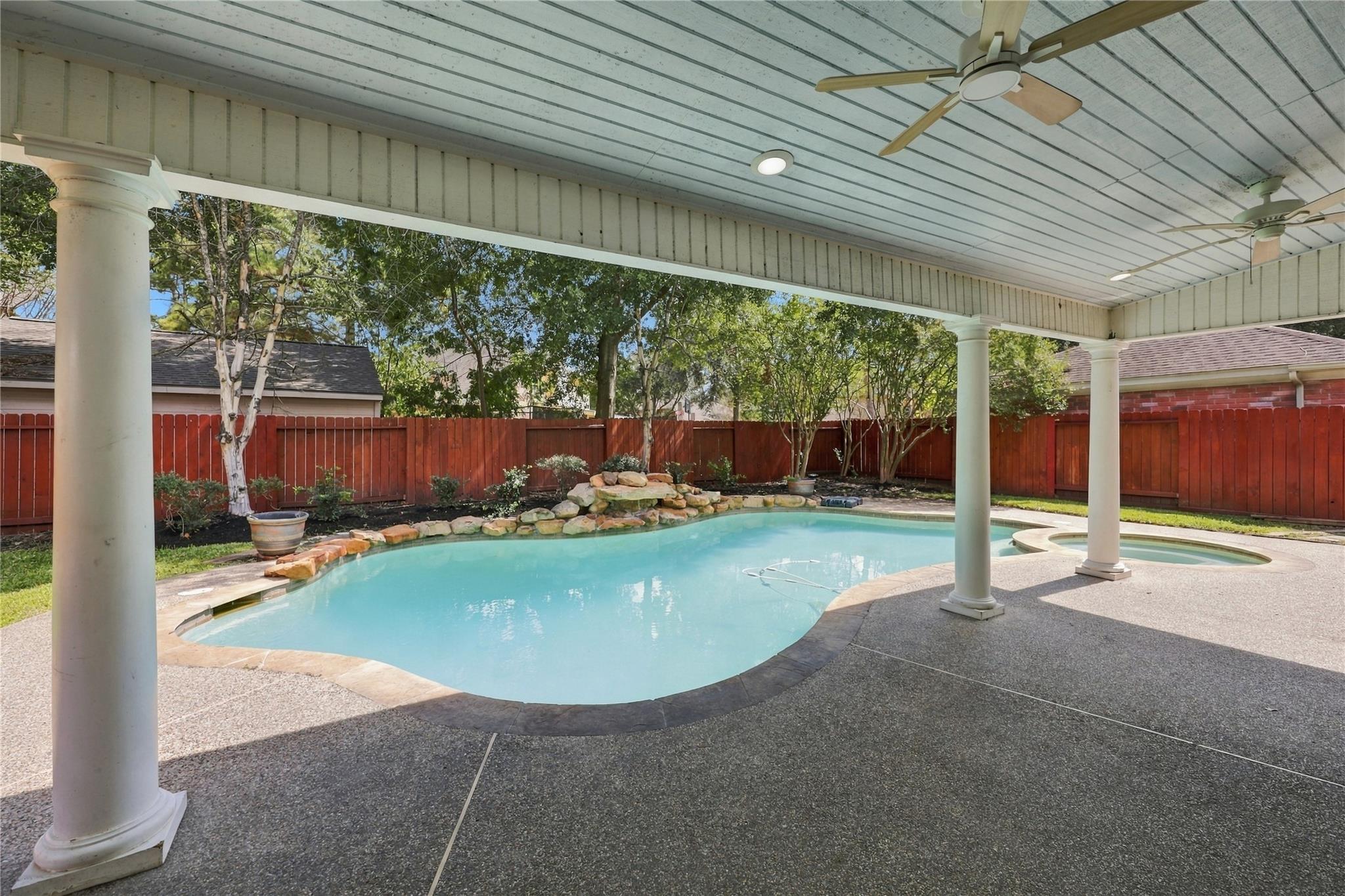 Backyard pool with a rock waterfall and attached spa beneath a covered patio.