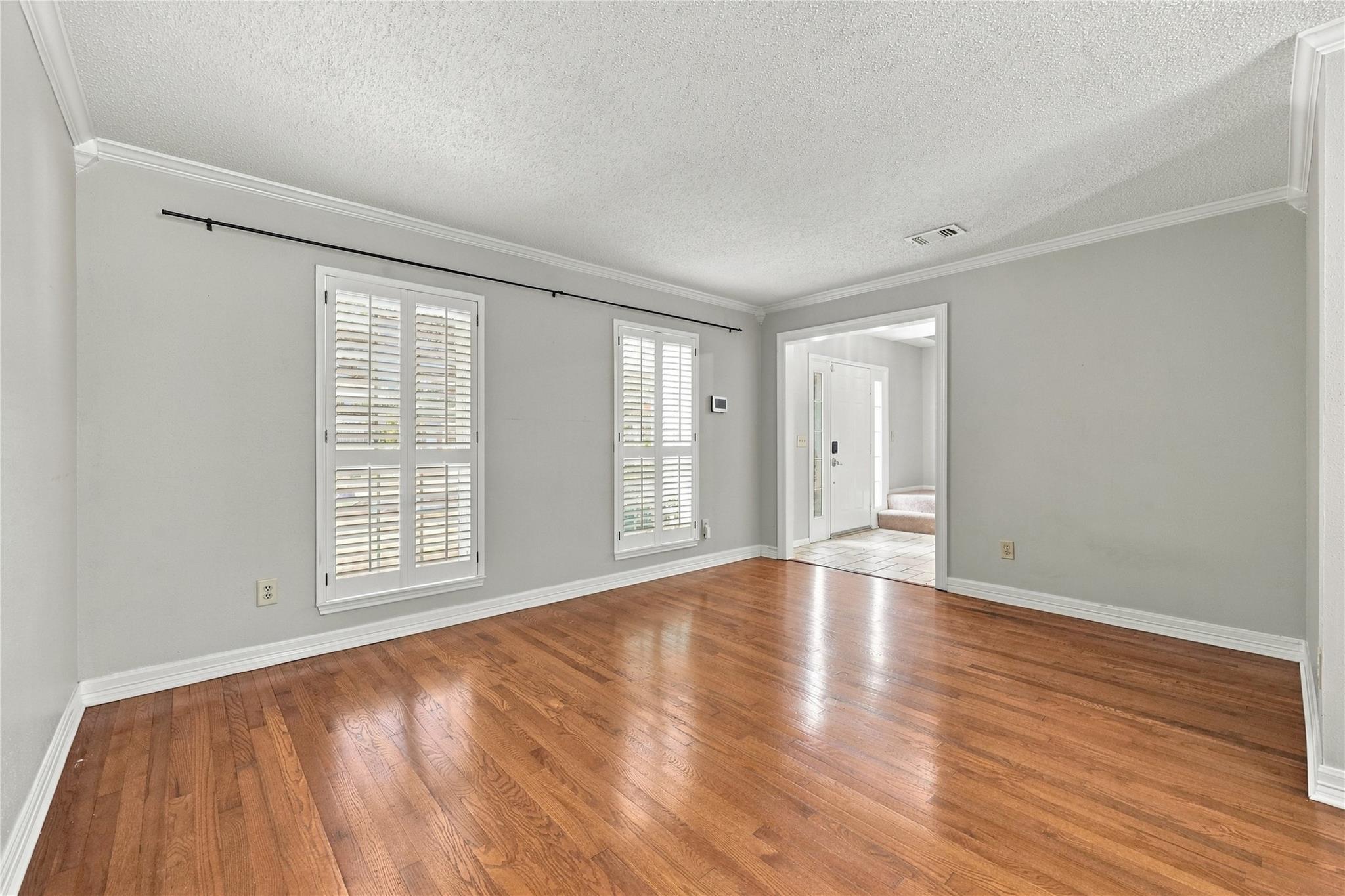Empty living room with polished hardwood floors and plantation shutters on two windows.