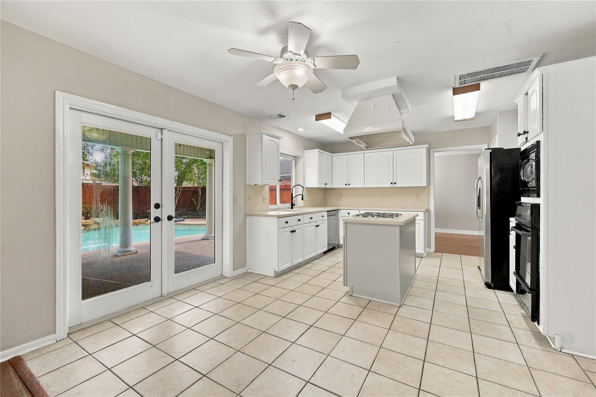 Kitchen with white cabinets and cooktop island; patio doors overlook a backyard pool.