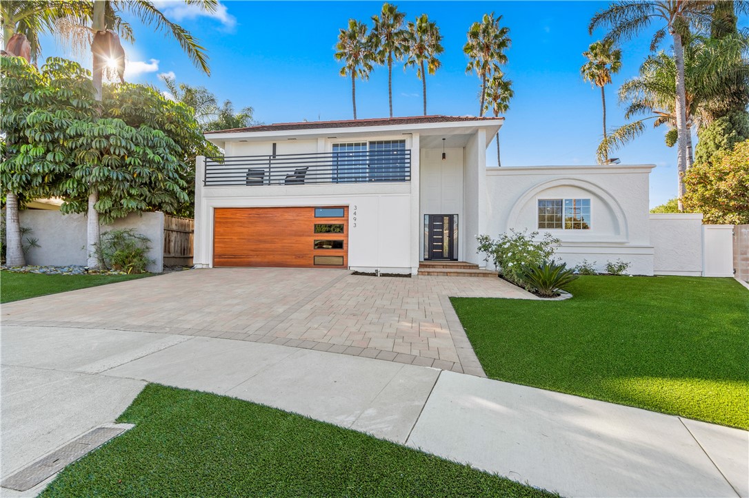 Modern white home with a wood-paneled garage door, balcony, and palm trees.