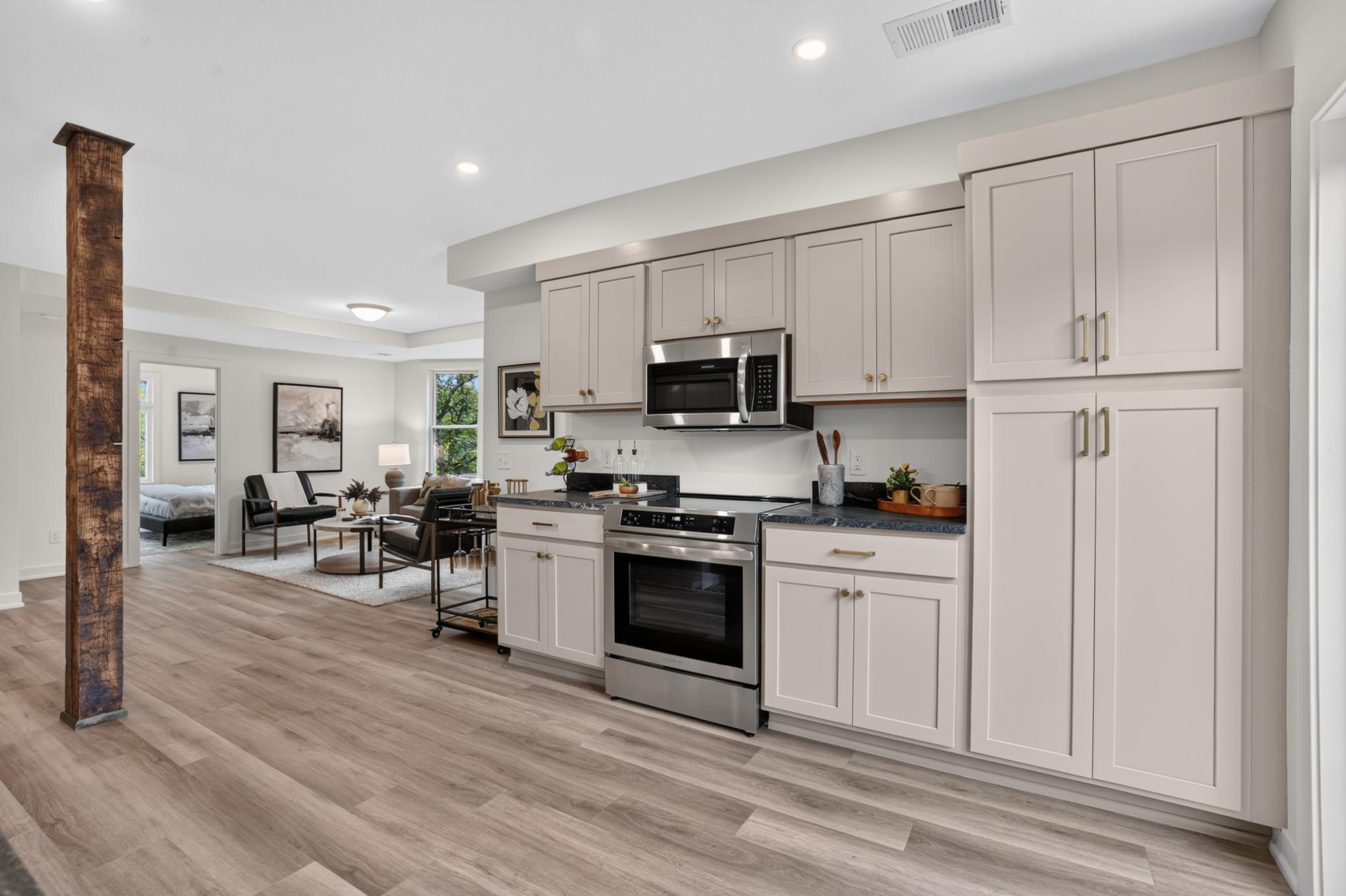 Kitchen with white cabinets and stainless appliances opening onto a furnished living area.