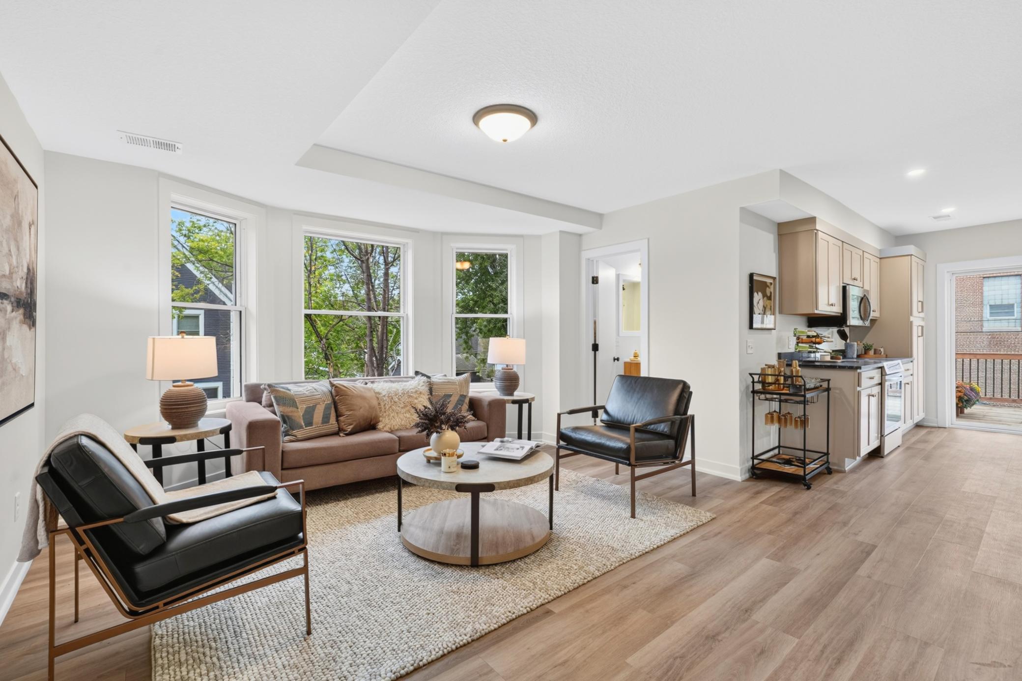 Open-plan living room and kitchen with large windows, neutral seating, and pale wood floors.
