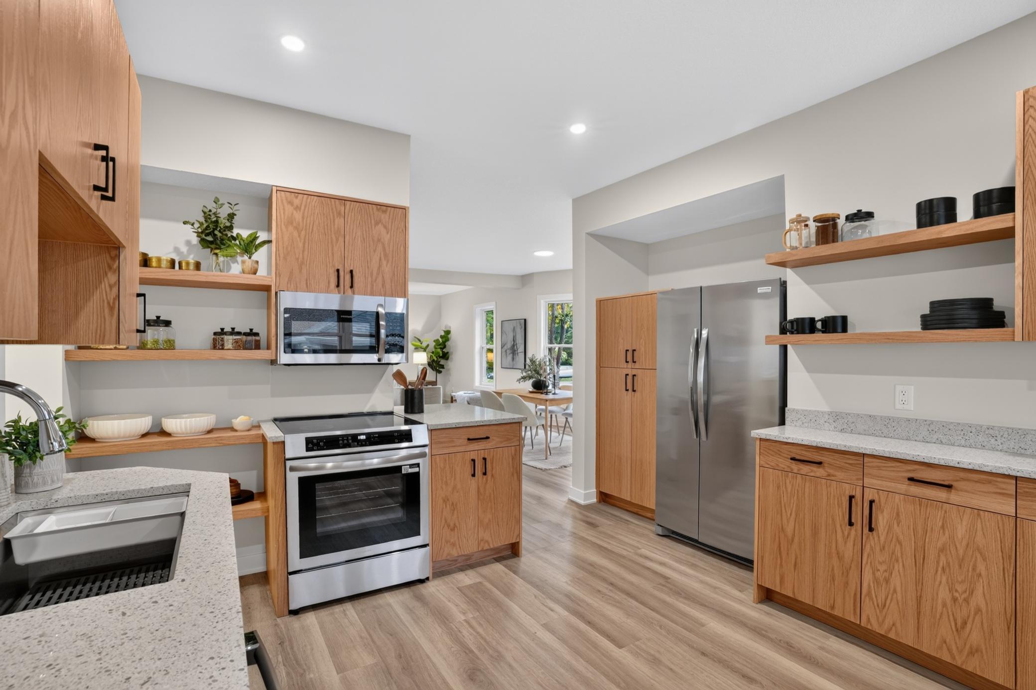 Kitchen with oak cabinets, open wood shelving, speckled counters, and stainless steel appliances.