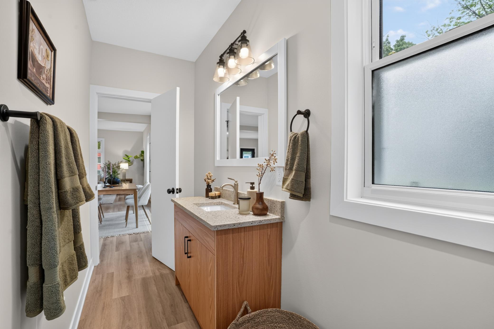 Bathroom with a wood vanity, speckled countertop, large mirror, and frosted-glass window.
