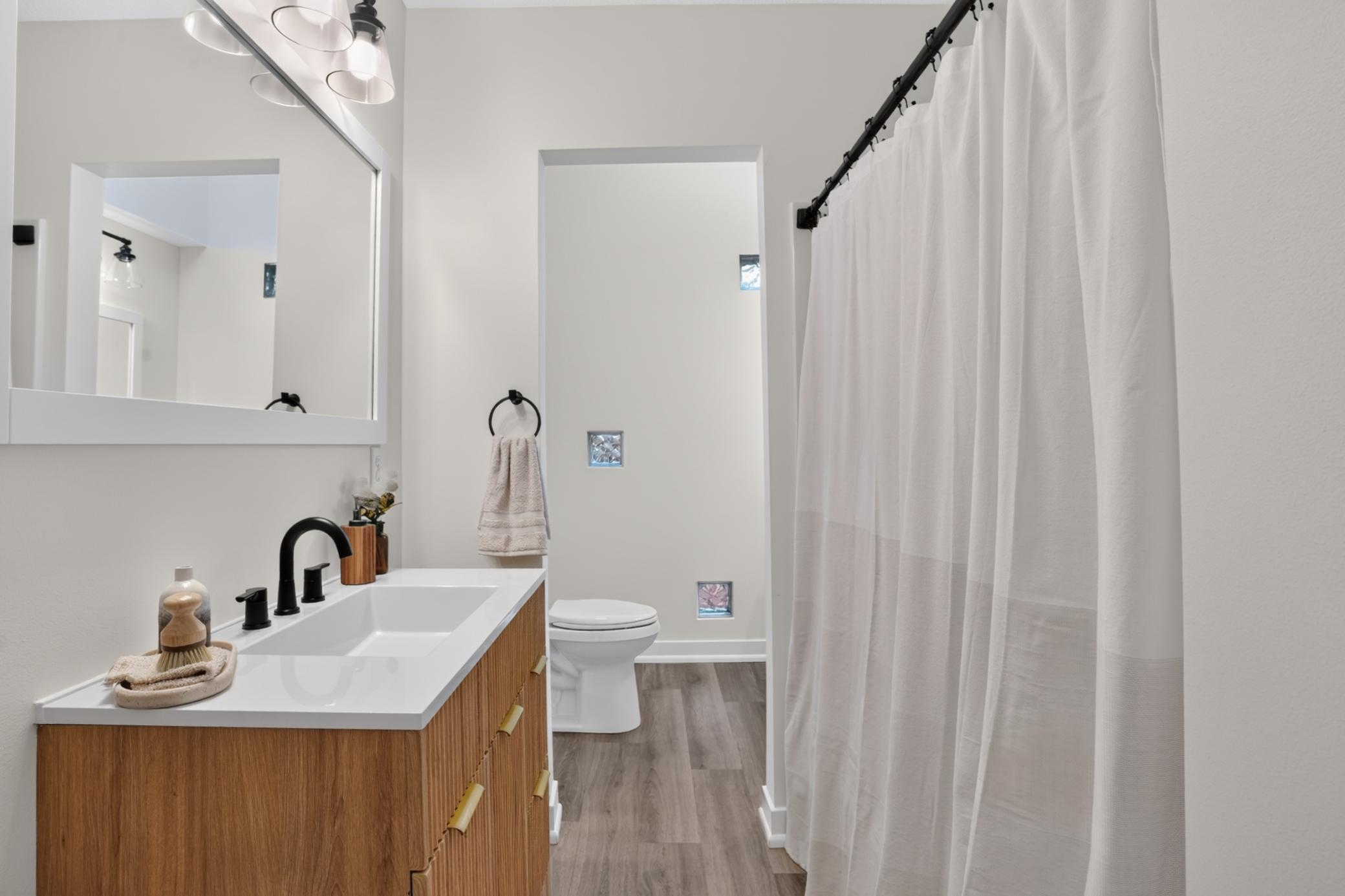 Bathroom with a wood vanity, black faucet, and white shower curtain.