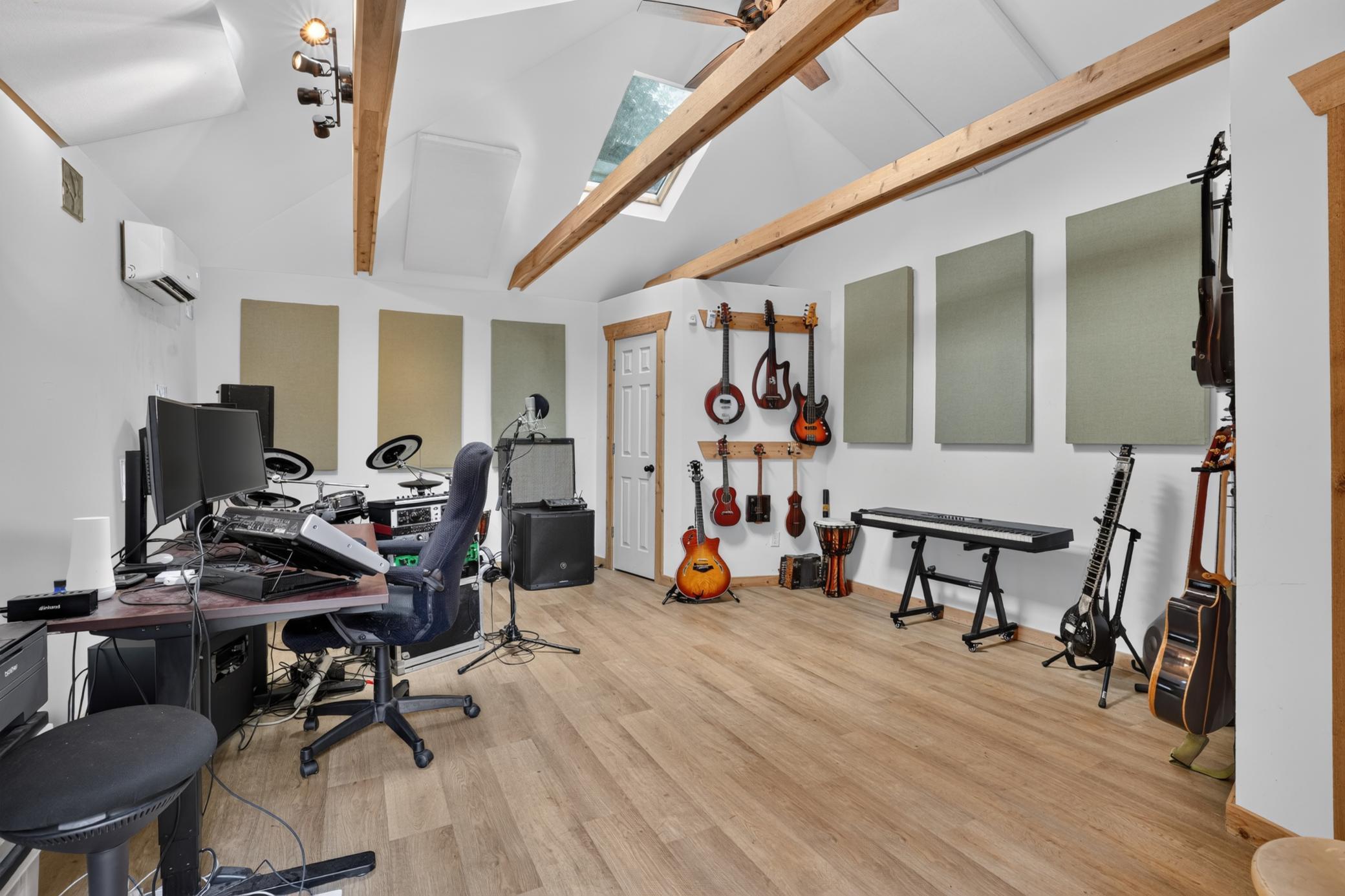 Music studio with guitars, keyboard, recording equipment, acoustic panels, and exposed ceiling beams.