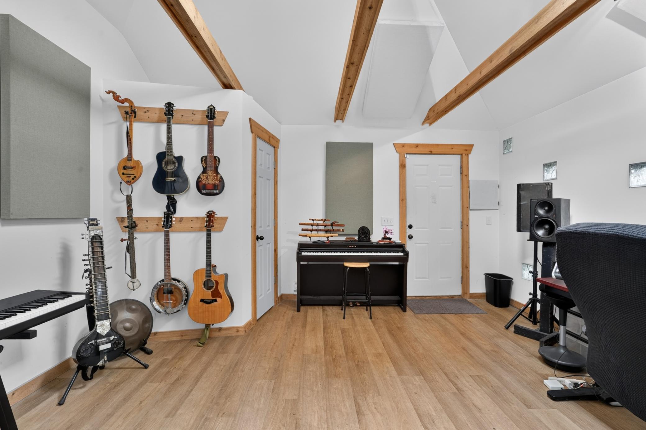 Music room with exposed wood ceiling beams, wall-mounted guitars, keyboards, and a piano.