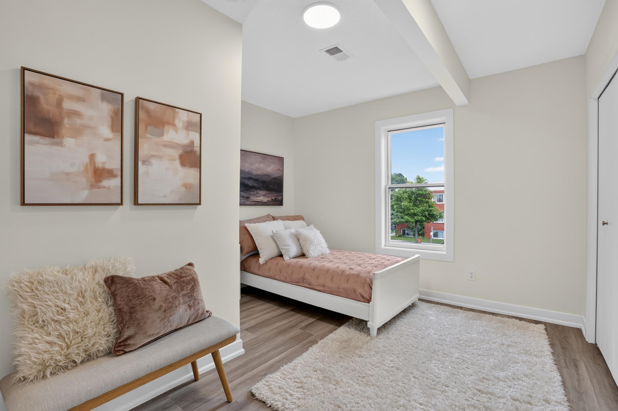 Furnished bedroom with a dusty rose daybed, cushioned bench, large rug, and sunny window.