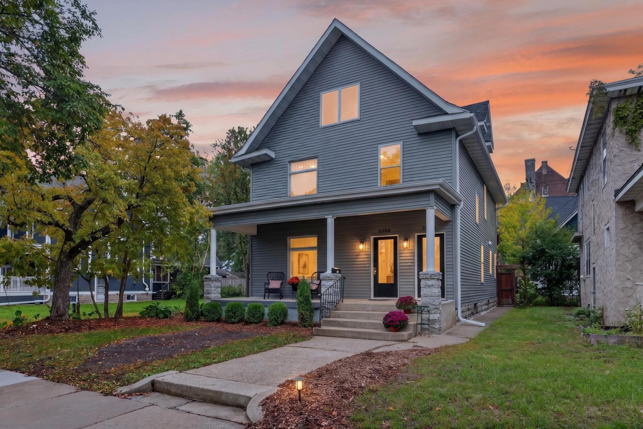 Gray two-story house with a covered porch and glowing windows at dusk.