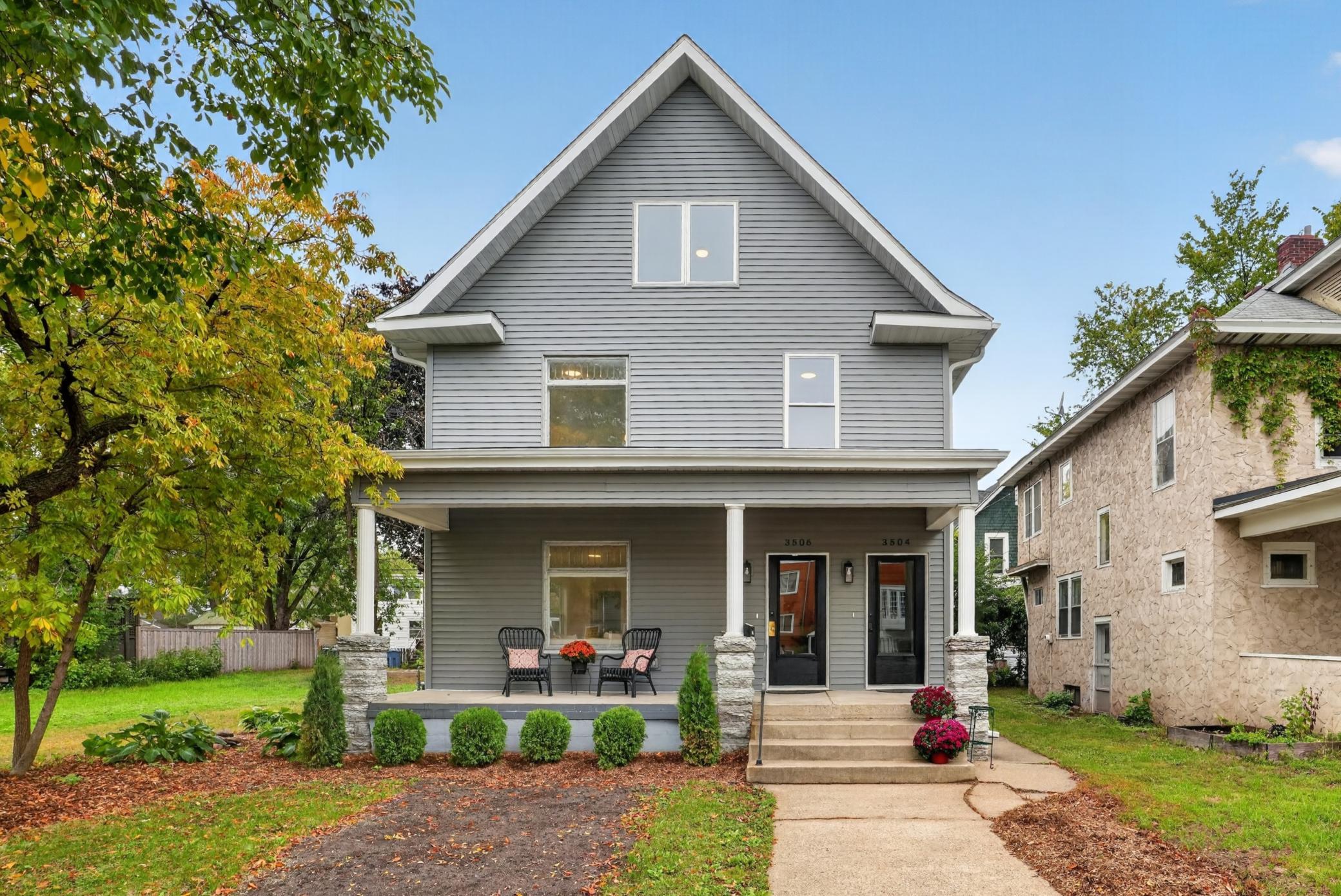 Gray two-story duplex with a steep gabled roof, covered porch, and autumn landscaping.