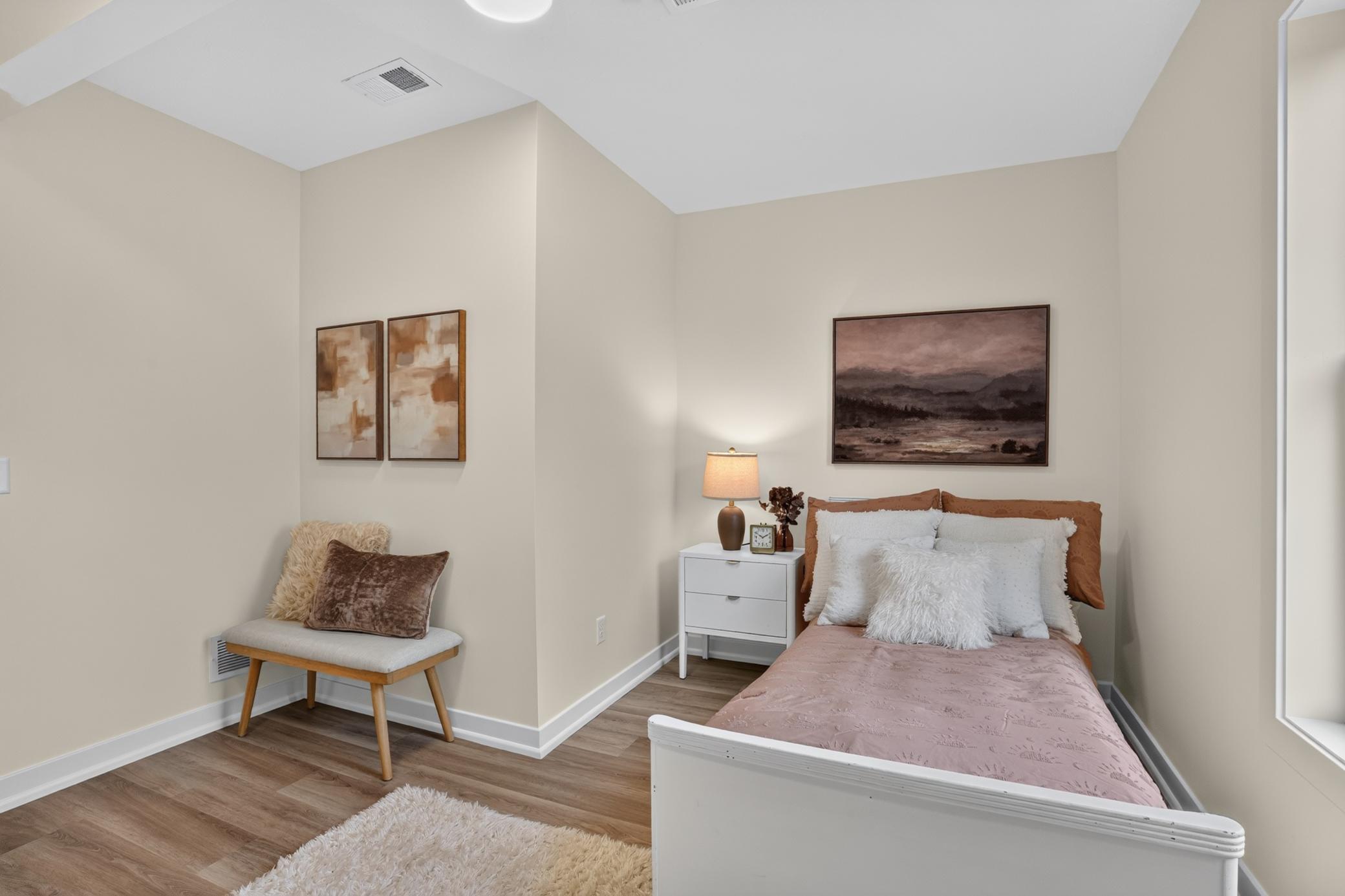 Staged bedroom with dusty-rose bedding, a white nightstand, and a cushioned bench.