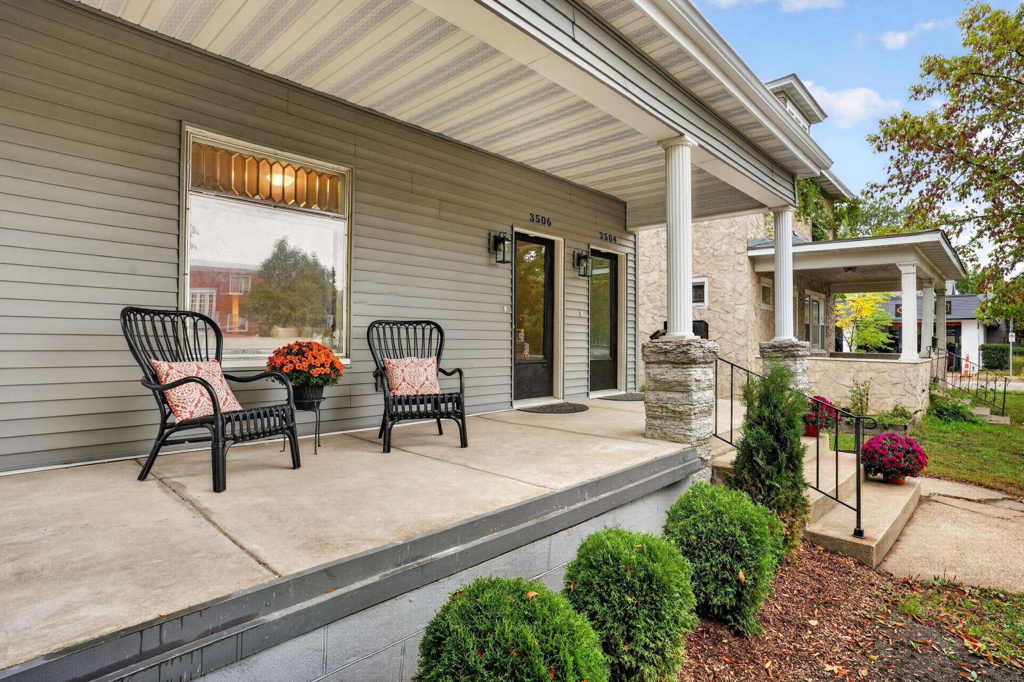 Covered front porch with two black chairs, white columns, and landscaped steps.