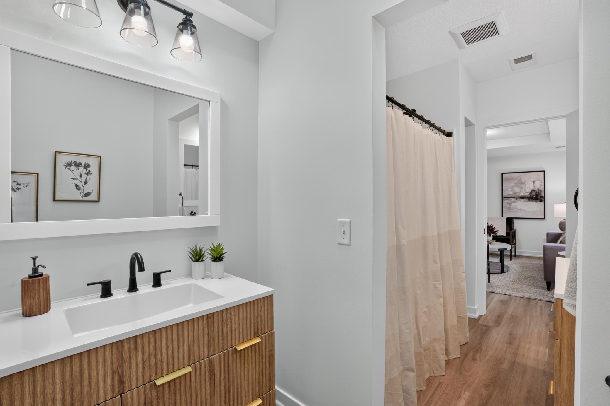Bathroom with a walnut-toned vanity, white sink, black faucets, and beige shower curtain.