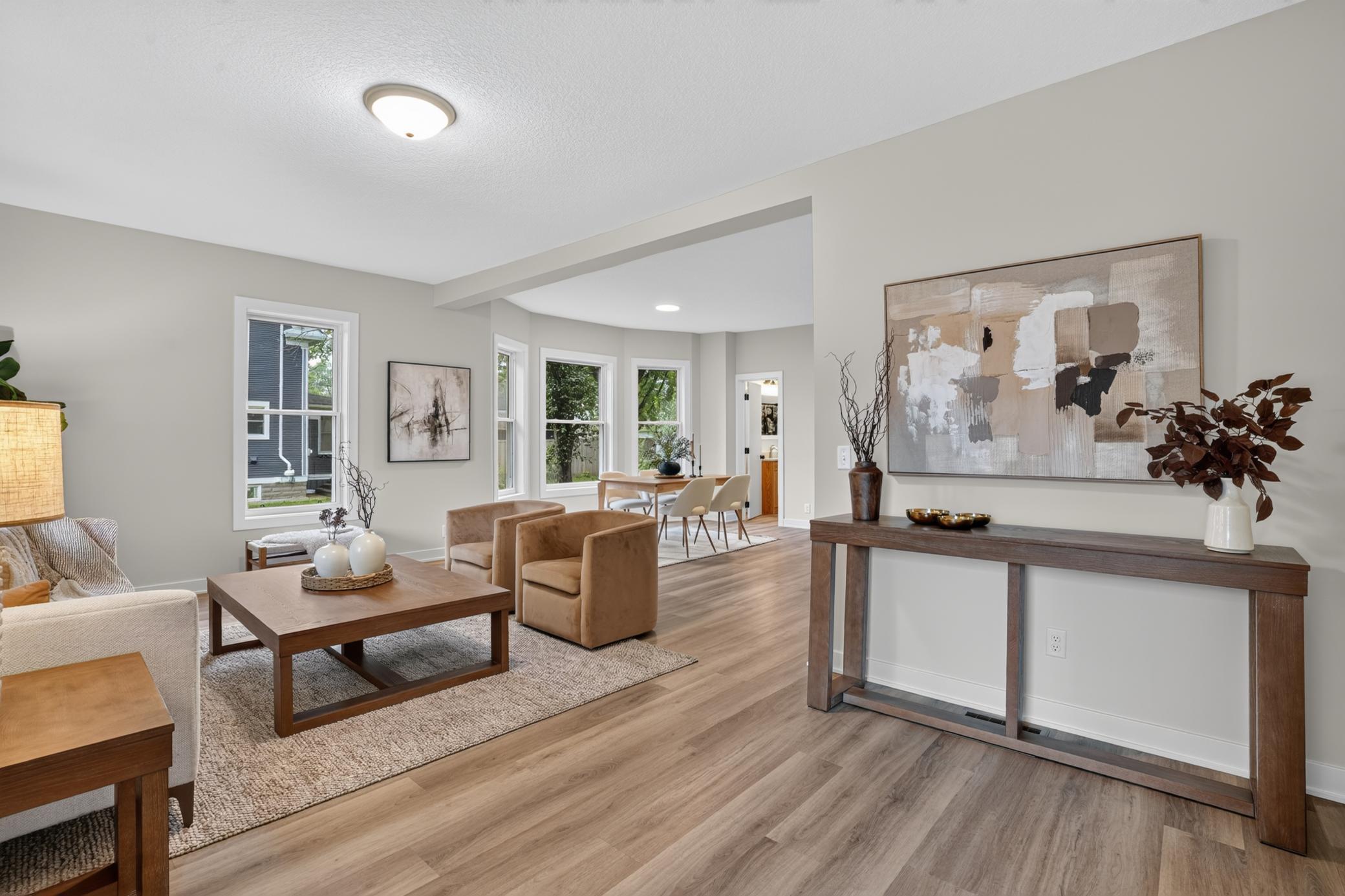 Staged open-plan living and dining area with tan armchairs, abstract art, and light wood floors.