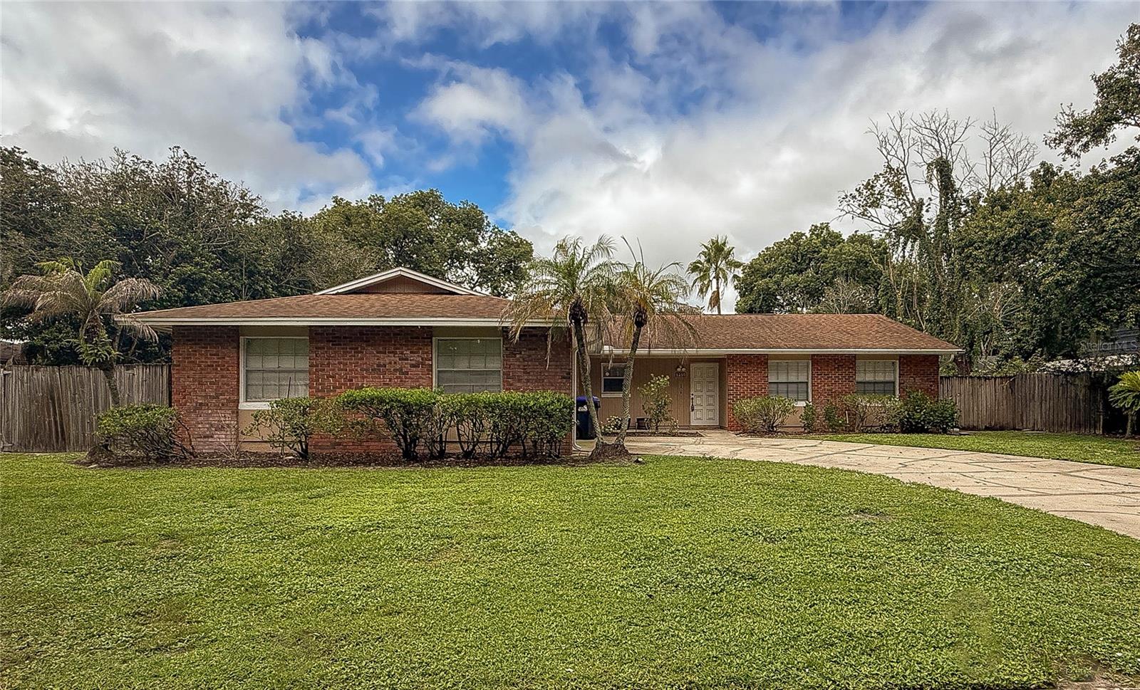 Single-story brick ranch with palm trees, a broad lawn, and a concrete driveway.