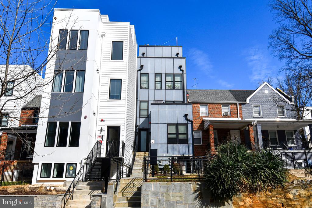 Modern white-and-gray attached home with front steps beside a traditional brick house.