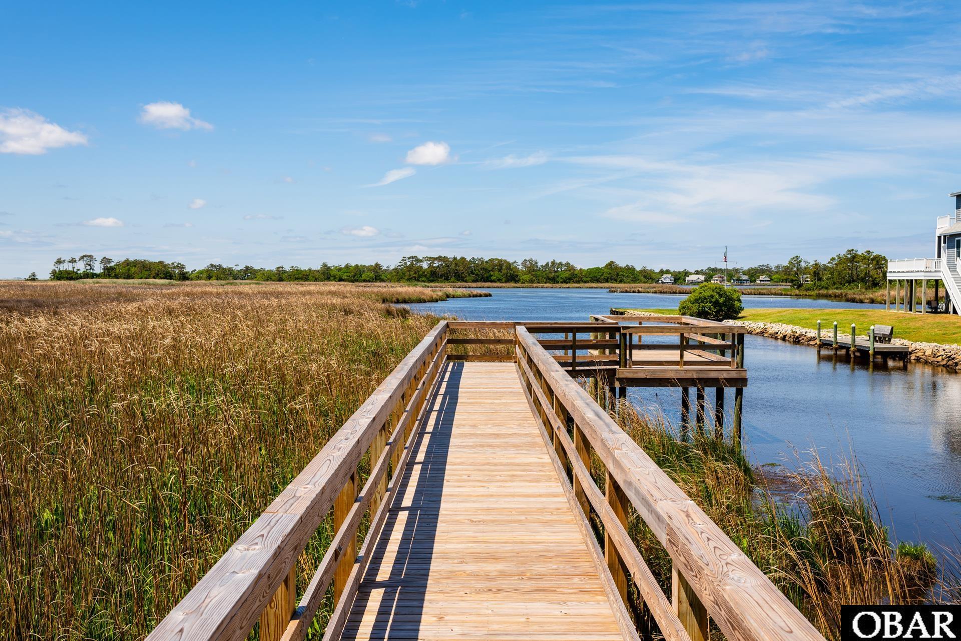 Wooden boardwalk and dock extending through marsh grass to a calm waterway.