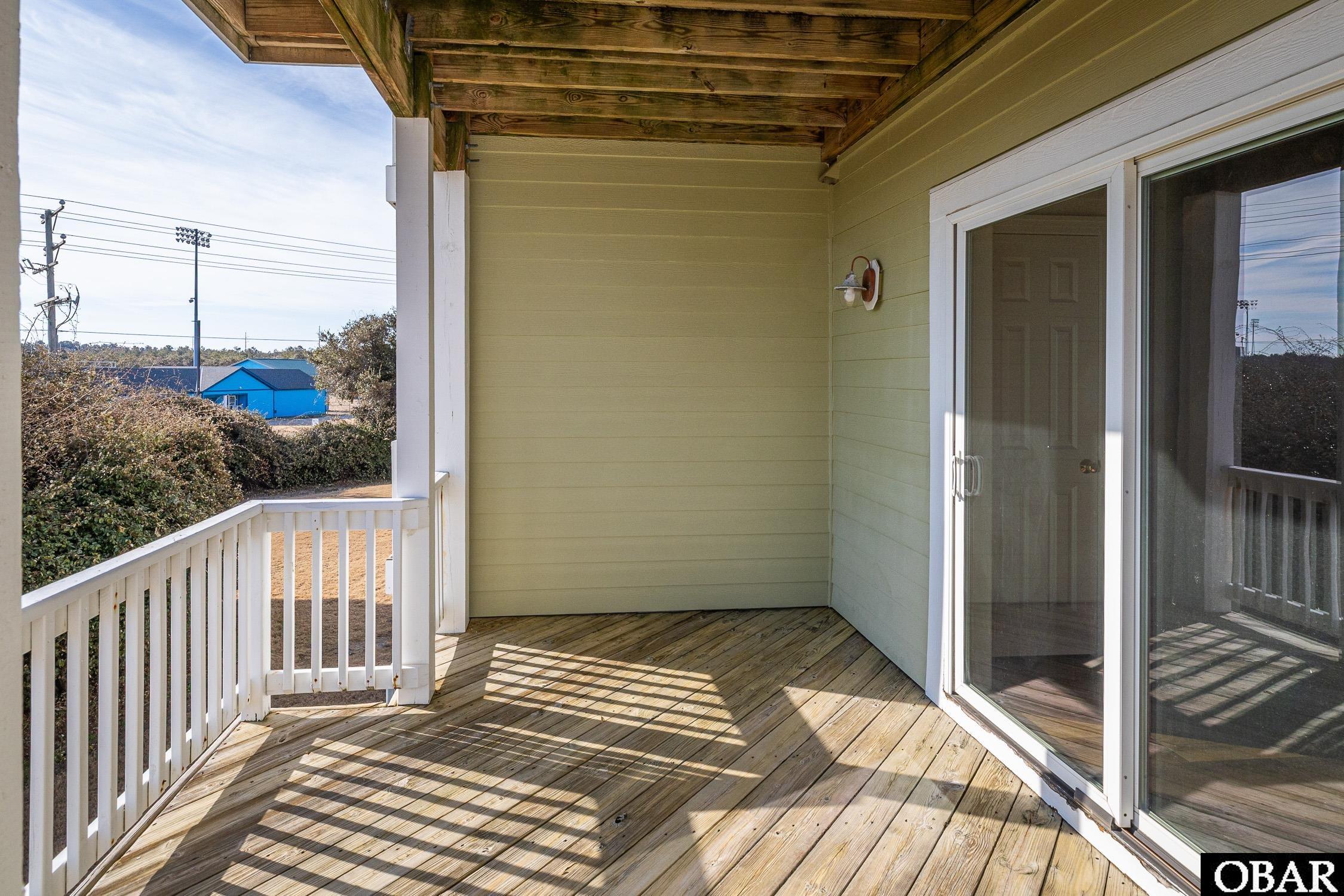 Covered wooden balcony with white railing and sliding glass doors.