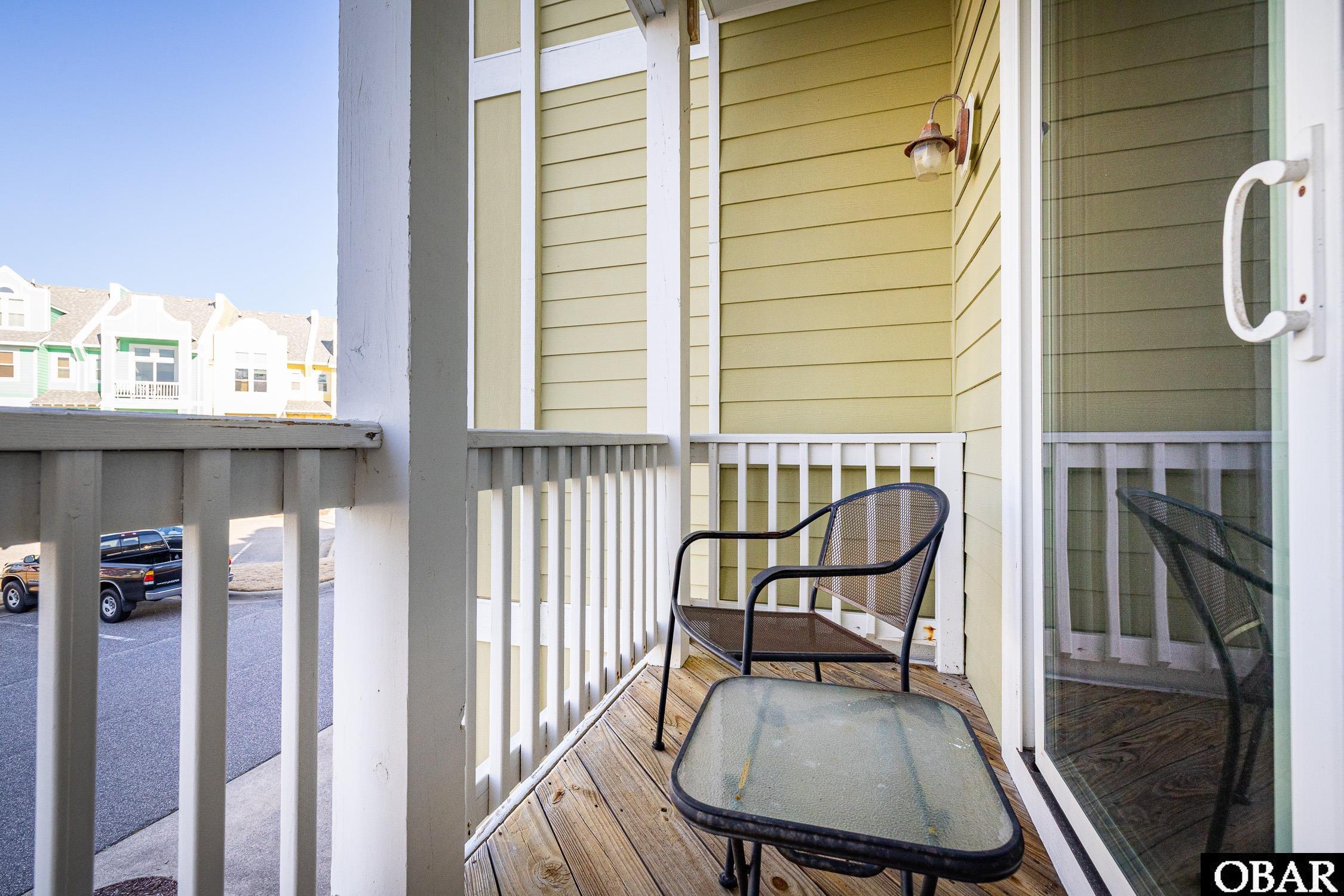 Balcony with a metal chair, glass-top table, and view of neighboring homes.
