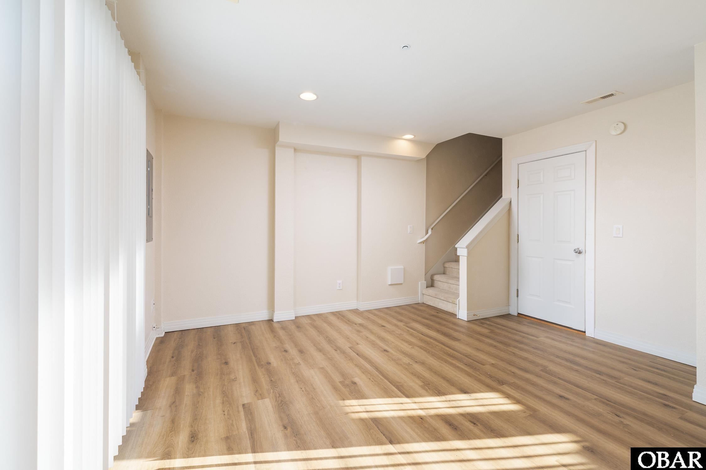 Vacant living area with wood-look floors, tall blinds, and a staircase.