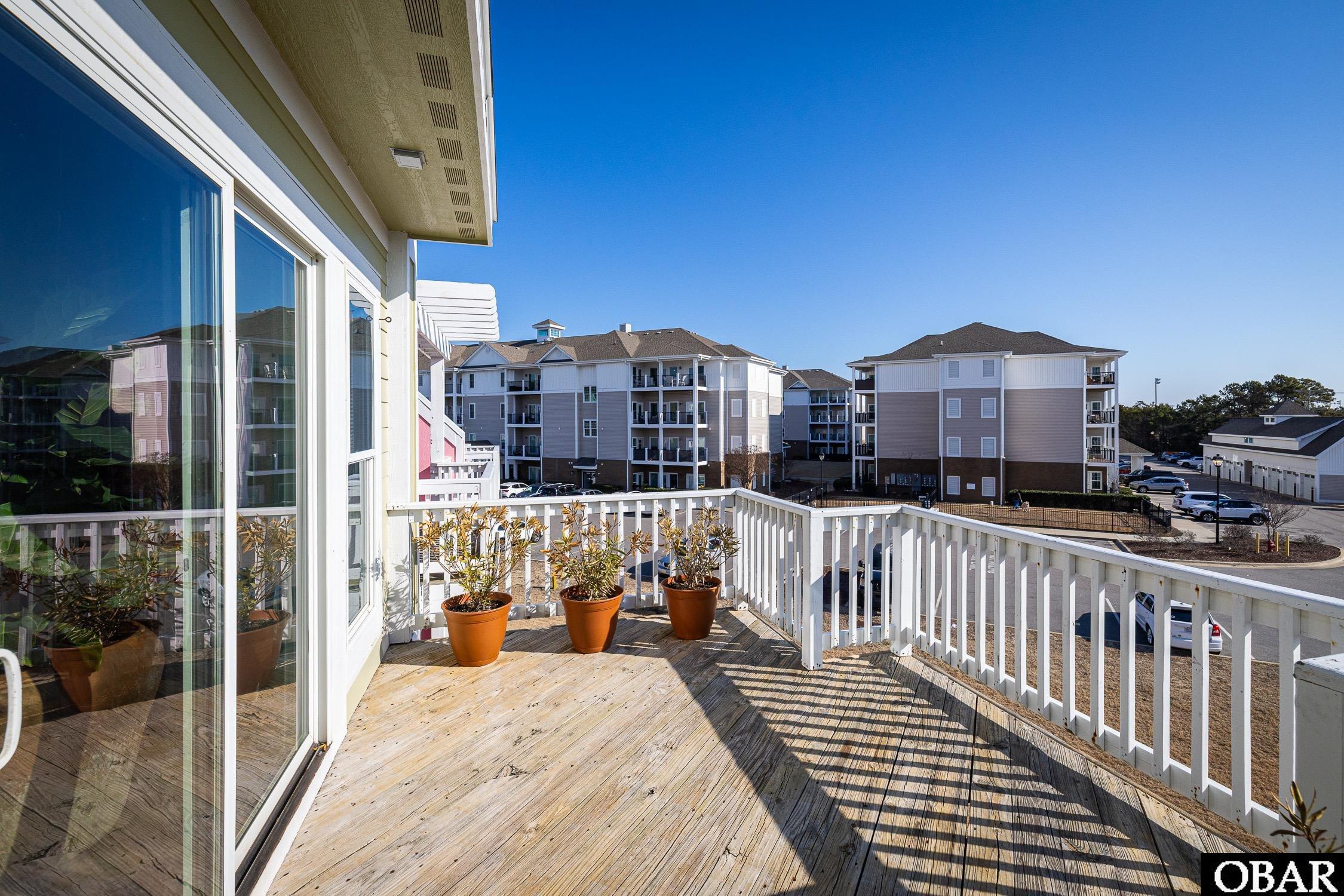 Condo balcony with a weathered wood deck, potted shrubs, and views of neighboring buildings.