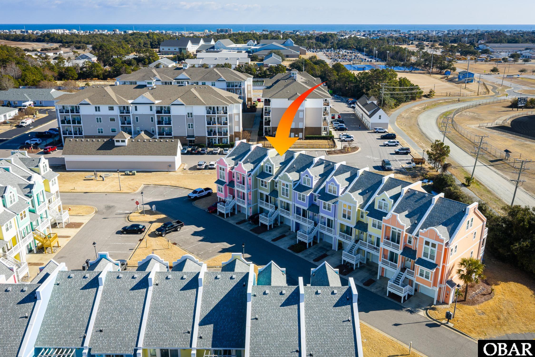 Aerial view of colorful coastal condominiums, with an orange arrow marking the featured unit and ocean beyond.